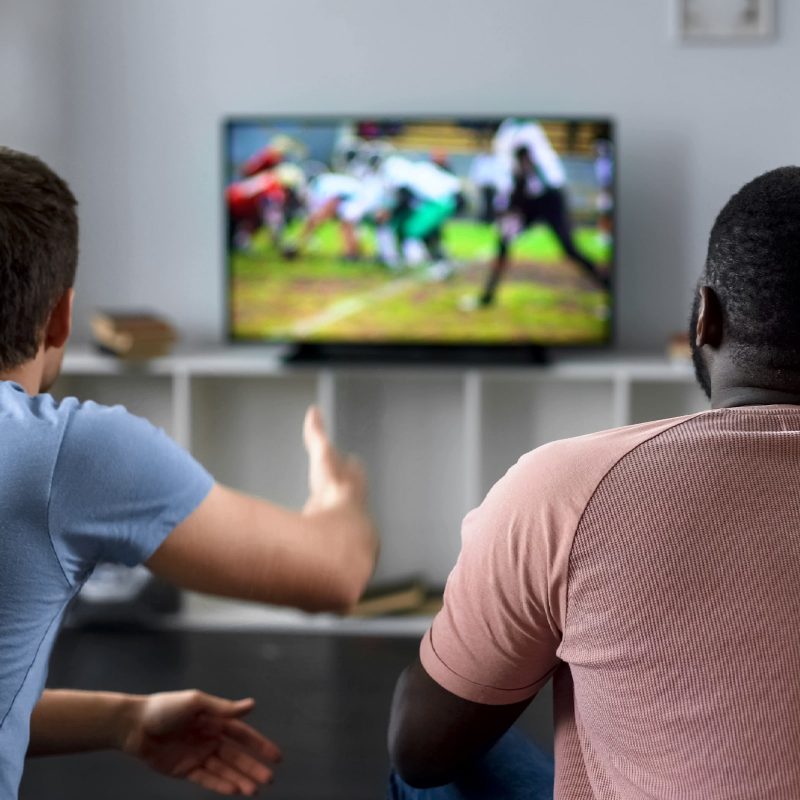 Two men sitting watch sports on TV