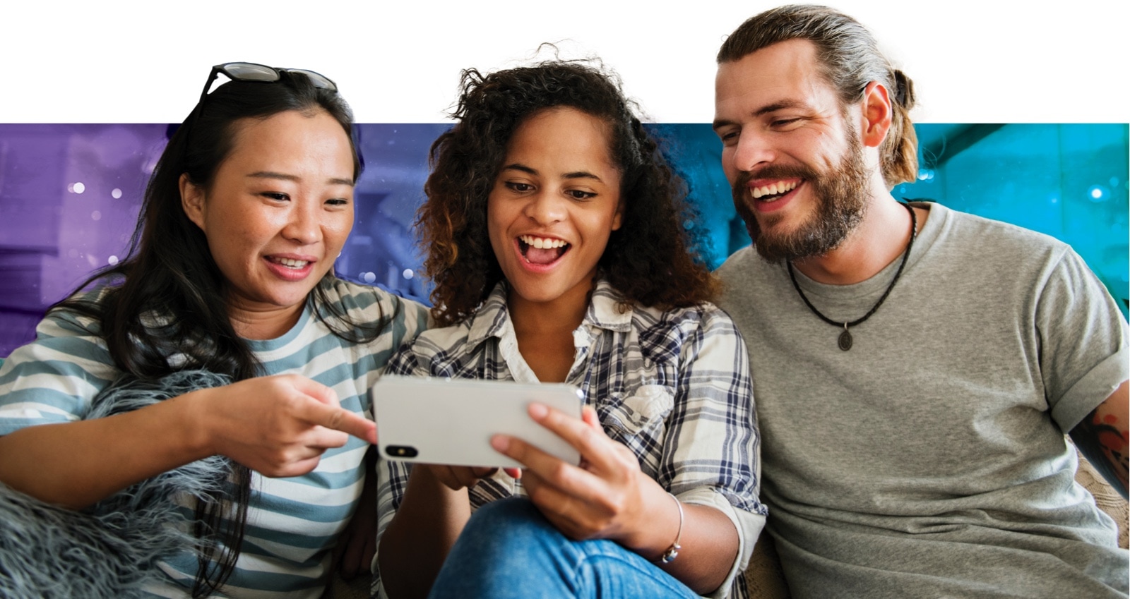 Two women and a man smiling while looking at a smartphone