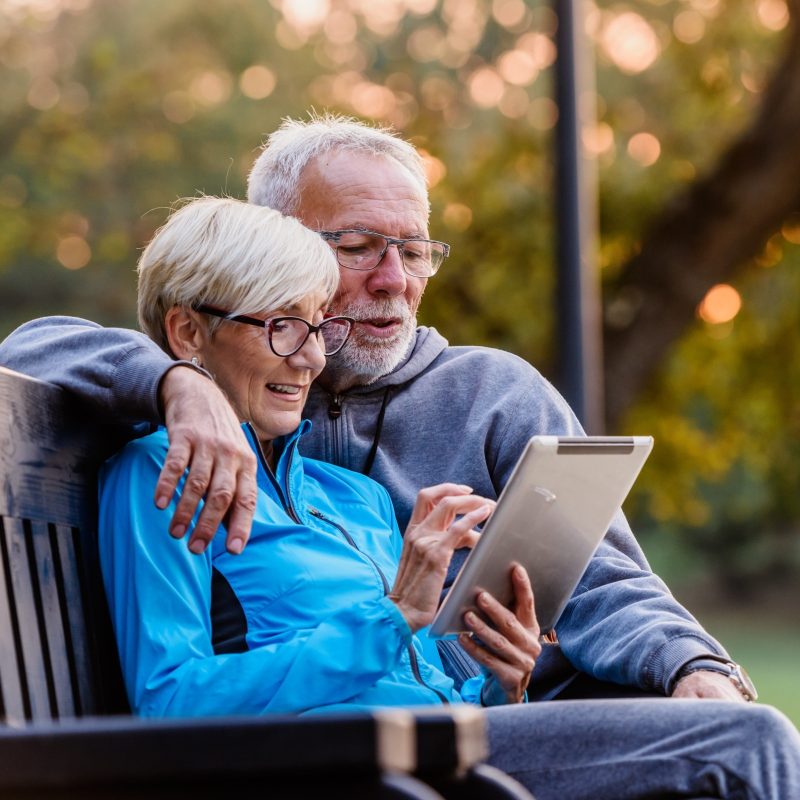 A senior couple sitting on a bench looking at a tablet device
